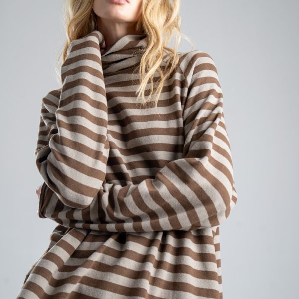 Sweter z golfem Mino Stripes delCane w beżowo-brązowe paski. Zbliżenie na sweter, modelka widoczna od ud w górę, jedną dłonią przytrzymuje górę golfu.
