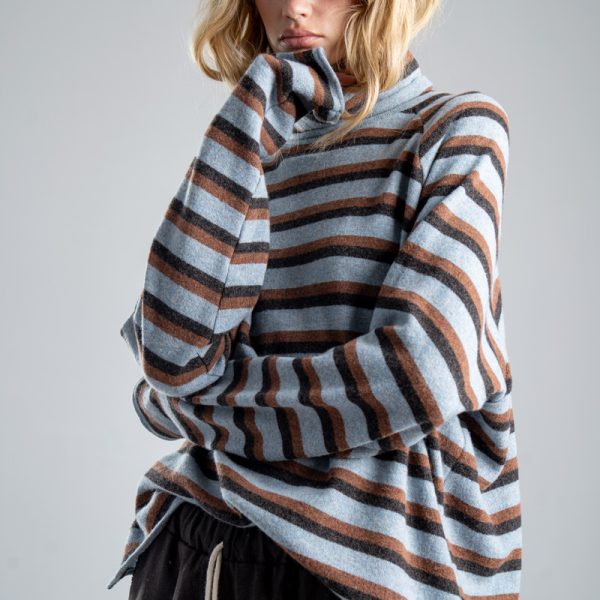 Sweter z golfem Mino Wool delCane w niebiesko-brązowe paski. Modelka widoczna od ud w górę, z sylwetką lekko skręconą w bok i dłonią podpierającą brodę.