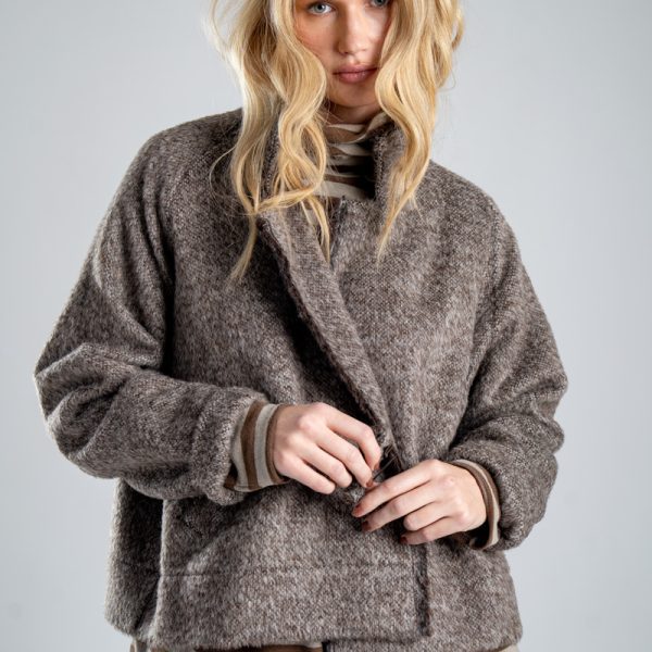 Kurtka Mino Wool delCane w brązowym melanżu. Zbliżenie od przodu, modelka widoczna od ud w górę, trzyma poły wełnianej kurtki, prezentując jej oryginalne zapięcie.