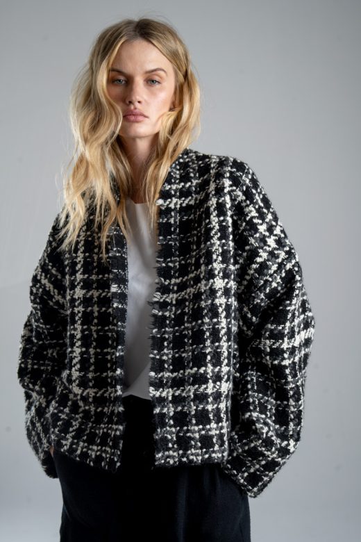 Kurtka kimono Mino Wool delCane w czarno-białym wzorze z szarymi akcentami. Modelka przodem, w ujęciu od bioder w górę, z rękami w kieszeniach spodni. Wyraźnie widoczny cały przód kurtki.
