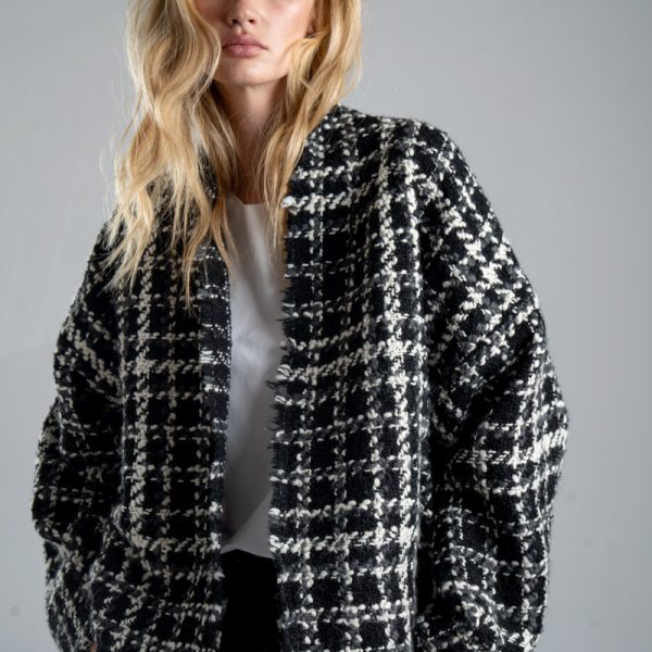 Kurtka kimono Mino Wool delCane w czarno-białym wzorze z szarymi akcentami. Modelka przodem, w ujęciu od bioder w górę, z rękami w kieszeniach spodni. Wyraźnie widoczny cały przód kurtki.