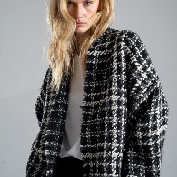 Kurtka kimono Mino Wool delCane w czarno-białym wzorze z szarymi akcentami. Modelka ustawiona lekko bokiem, patrzy w obiektyw, trzymając ręce w kieszeniach spodni. Ujęcie od bioder w górę.