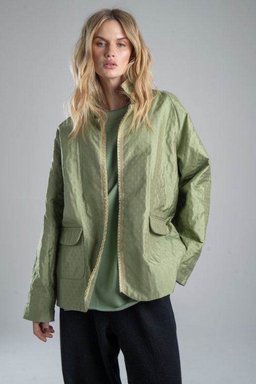 Marynarka Mino Green delCane w miętowym odcieniu zieleni, z delikatnym wzorem żakardowym. Modelka przodem, widoczna od uda w górę, patrzy w obiektyw. Jedną rękę trzyma w kieszeni spodni, drugą opuszcza wzdłuż ciała.