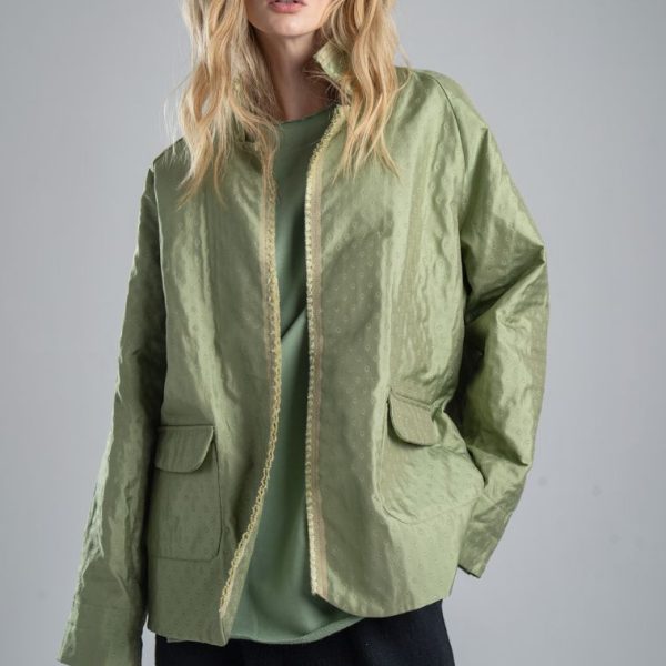 Marynarka Mino Green delCane w miętowym odcieniu zieleni, z delikatnym wzorem żakardowym. Modelka przodem, widoczna od uda w górę, patrzy w obiektyw. Jedną rękę trzyma w kieszeni spodni, drugą opuszcza wzdłuż ciała.