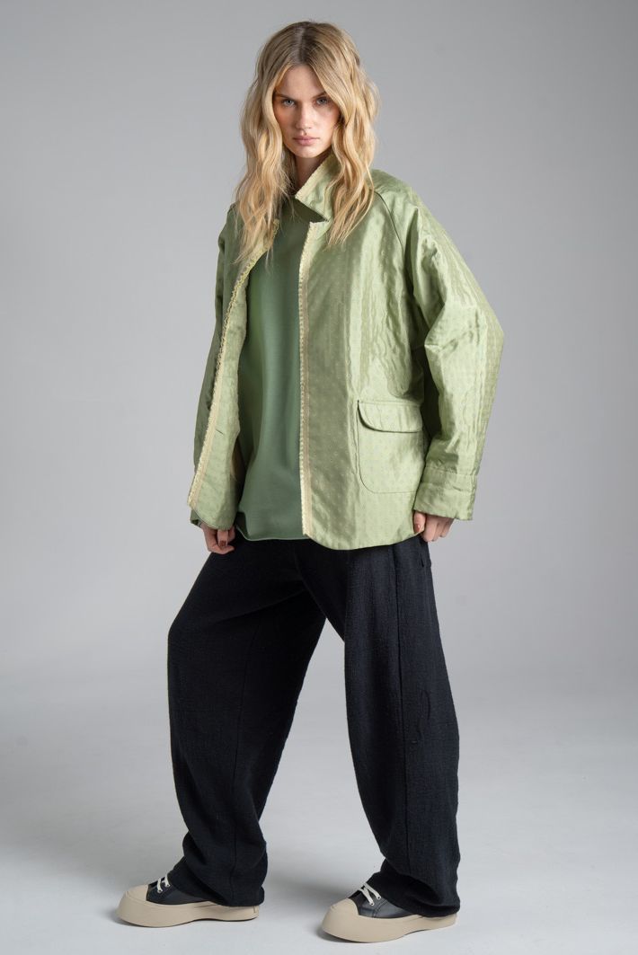 Marynarka Mino Green delCane w miętowym odcieniu zieleni. Modelka w pełnej sylwetce, ustawiona przodem pod lekkim kątem, z jedną nogą wysuniętą w bok. Patrzy w obiektyw.
