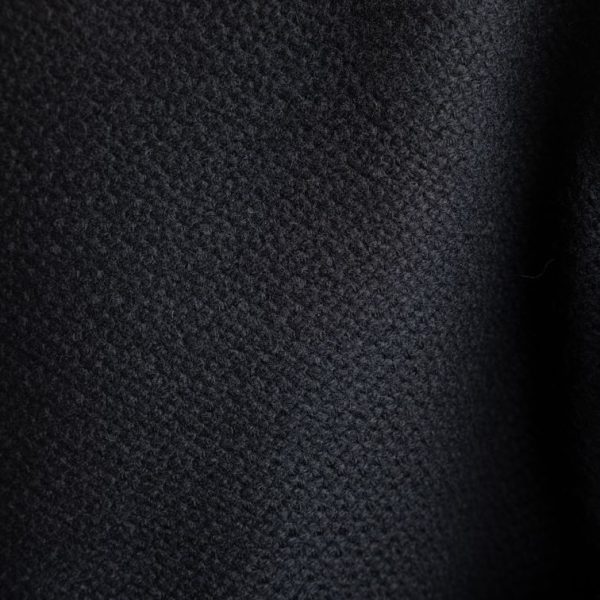 Zbliżenie na grubą, gęsto tkaną wełnę marynarki Mino Noir delCane. Wyraźnie widoczna zwarta faktura materiału i głęboki odcień czerni.