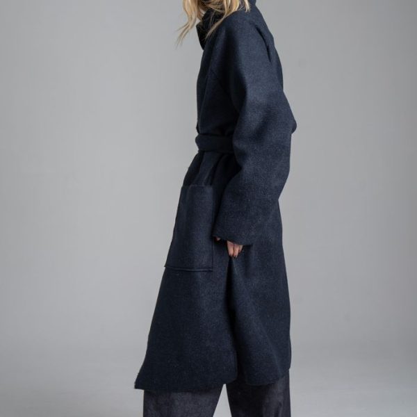 Płaszcz Mino Wool delCane w głębokim odcieniu granatu. Modelka w pełnej sylwetce, ustawiona bokiem, prezentuje płaszcz zawiązany paskiem.