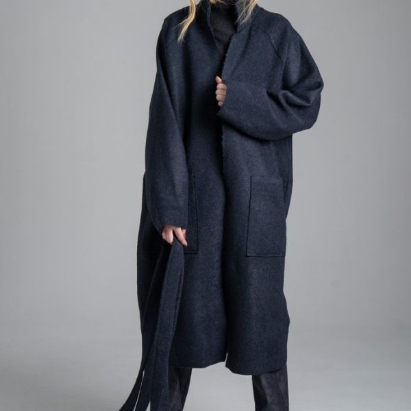 Granatowy płaszcz Mino Wool delCane, modelka przodem, cała sylwetka. Płaszcz rozwiązany, modelka jedną ręką przytrzymuje jego przód, a w drugiej trzyma pasek.