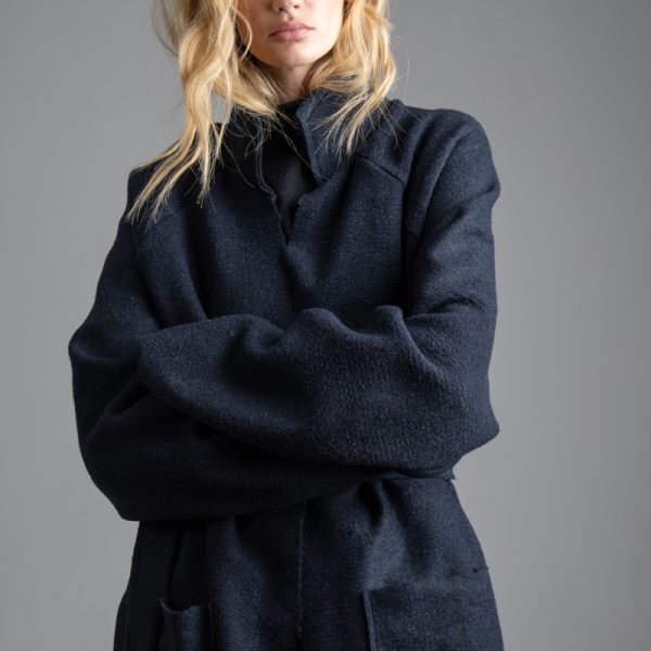 Granatowy płaszcz Mino Wool delCane, modelka przodem, w ujęciu od uda w górę, z rękami splecionymi z przodu. Wyraźnie widoczna faktura wełny i kolor płaszcza.