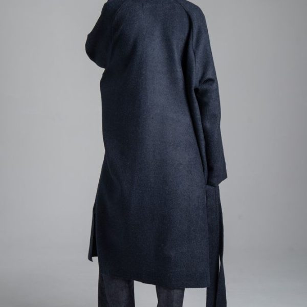 Granatowy płaszcz Mino Wool delCane, widok od tyłu. Modelka w pełnej sylwetce, w swobodnej pozie, trzyma w jednej ręce rozwiązany pasek płaszcza.
