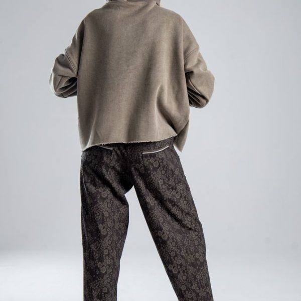 Spodnie Mino Jacquard delCane z włoskiego żakardu o subtelnym, rozmytym wzorze. Modelka tyłem, w pełnej sylwetce, z jedną nogą lekko wysuniętą w bok. Wyraźnie widoczny tył spodni.