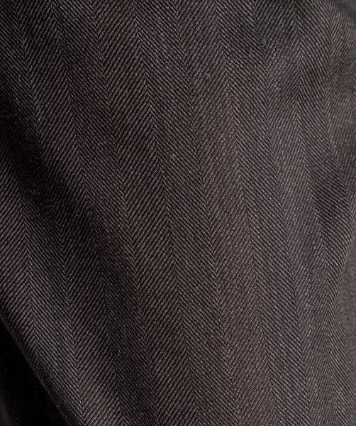 Zbliżenie na wełnianą tkaninę spodni Mino Wool delCane. Wyraźnie widoczna faktura wełny, subtelny wzór jodełki i ciemny odcień brązu.